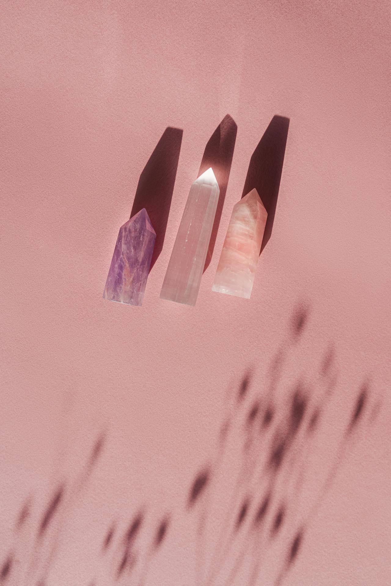 Three pointed crystals casting shadows on a soft pink surface